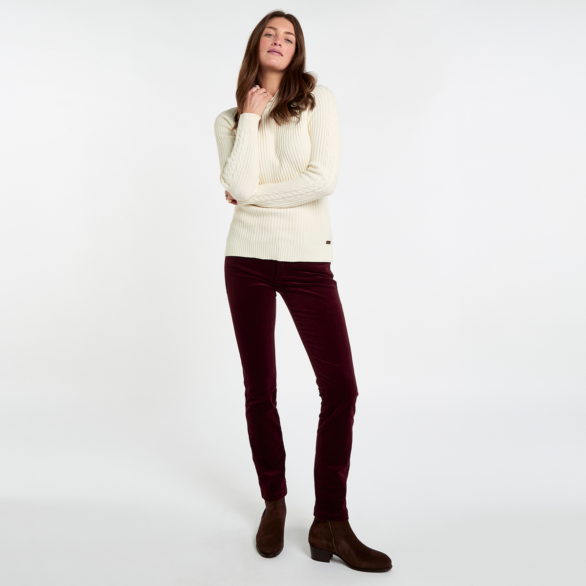 Woman wearing Dubarry Honeysuckle Pincord Trousers in Raisin with a cream knitted jumper and brown ankle boots.