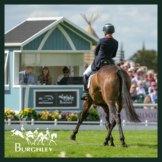 Equestrian rider competing on horseback at the Burghley Horse Trials, with spectators and Defender branding in the background.