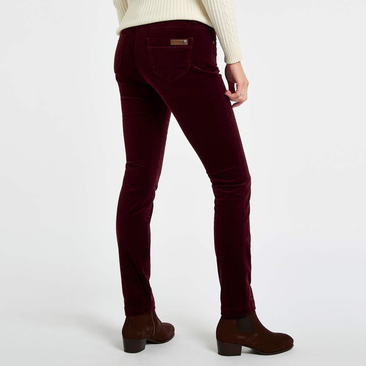 Rear view of a woman wearing Dubarry Honeysuckle Pincord Trousers in Raisin with brown ankle boots, showing the slim fit and rear pockets.