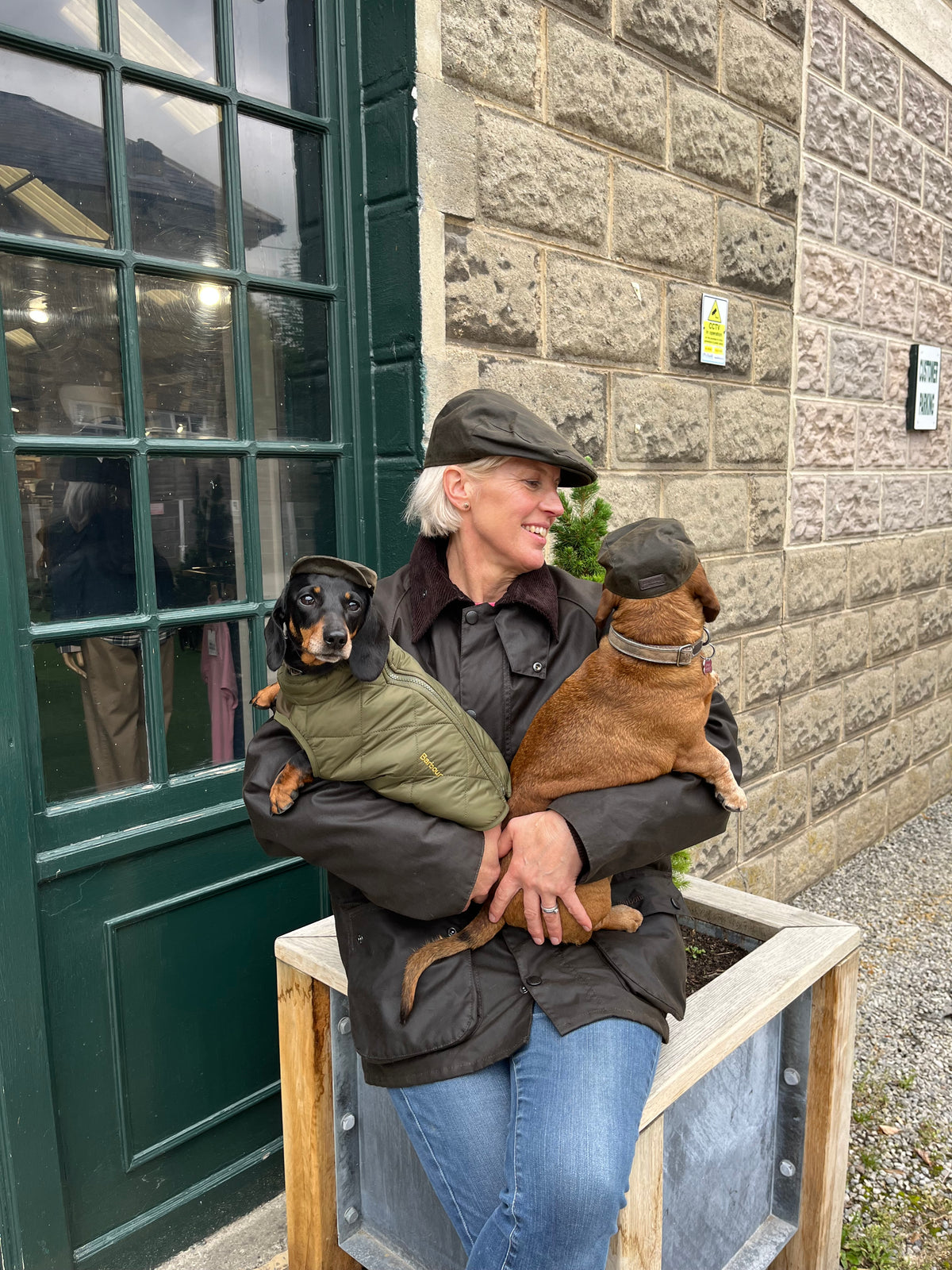 Melanie Brocklehurst outside the Sporting Showroom holding Doris and Dora - wearing Barbour coats and caps.