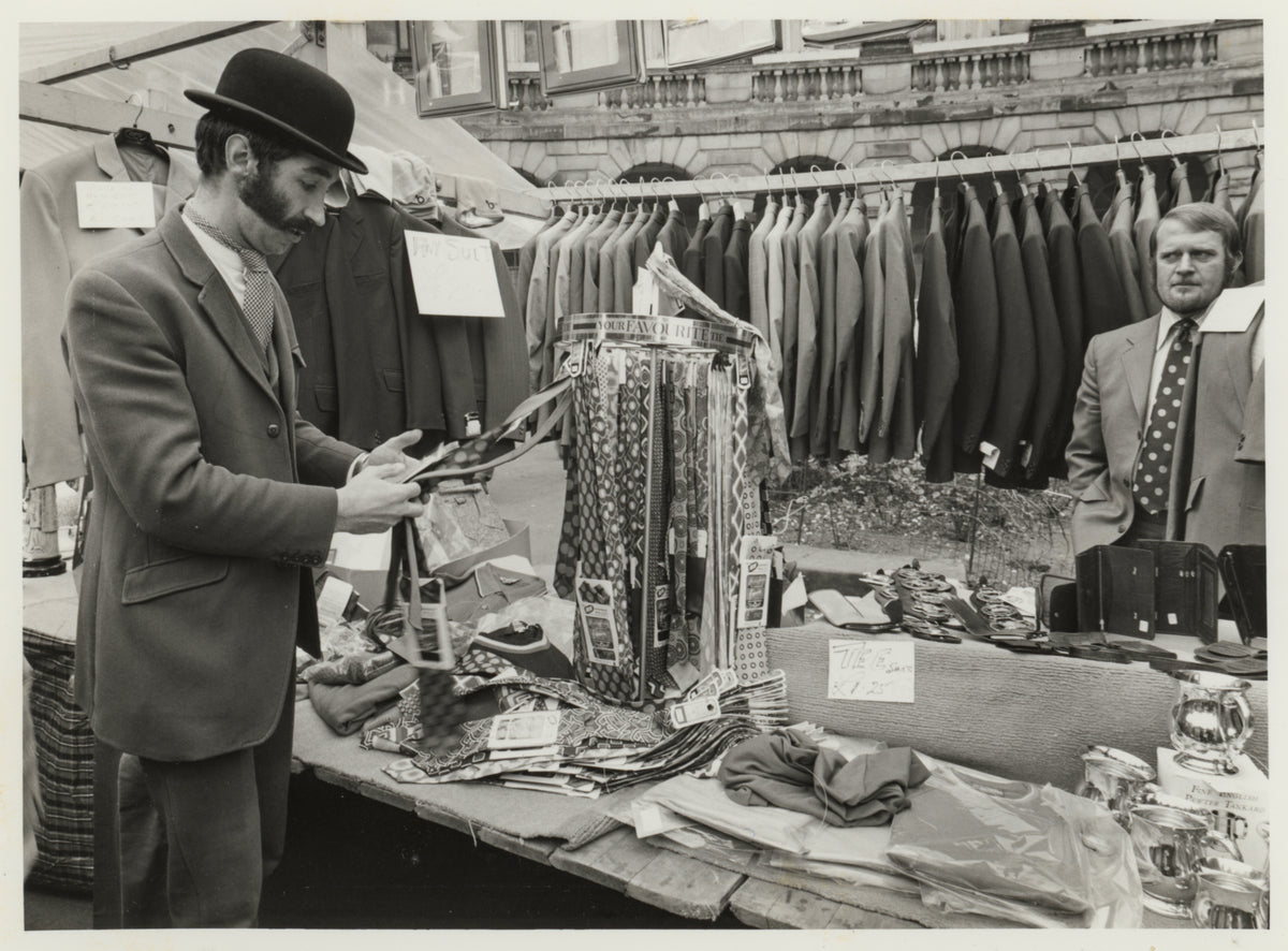 Archive photograph of John Brocklehurst and Bill Kreuger on the Brocklehursts stand at a country show, surrounded by suits, ties and country clothing for sale.