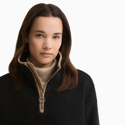 Close-up of a woman wearing the Barbour Bamburgh Fleece in Black, with the tan-trimmed collar open over a cream roll-neck jumper.