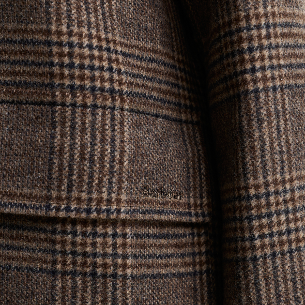 Close-up of the brown Prince of Wales check pattern with a subtle Barbour logo embroidered on the pocket flat.