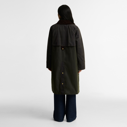 Model viewed from the back wearing the Barbour Kirklees Checked Waxed Jacket. A longline fern green waxed cotton coat with a dark brown corduroy collar and brass buttons.