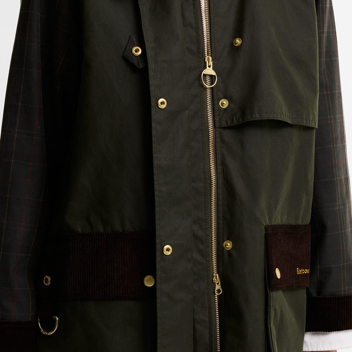 Close-up of the Barbour Kirklees Checked Waxed Jacket in fern green. Featuring brass stud fastenings and a two-way zip. The pockets and cuffs are finished with a brown corduroy trim and the sleeves showcase a checked pattern.