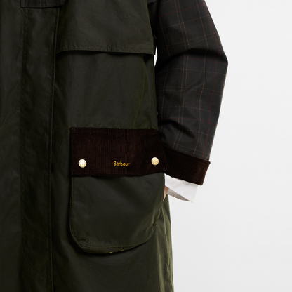 A close-up of the Barbour Kirklees Check Waxed Jacket in fern green, showcasing the side entry to the pocket.  With brown corduroy trim on the pocket and cuffs, and brass-tone snap buttons. The Barbour logo is embroidered on the pocket flap and the sleeves feature a checked pattern. 