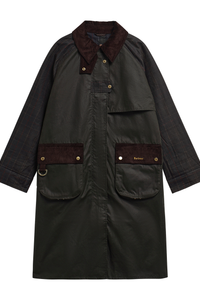 The Barbour Kirklees Checked Waxed jacket is a longline waxed cotton jacket in fern green with dark brown corduroy collar and pocket flaps, featuring brass-tone snap buttons and a Barbour logo on the pocket flap.