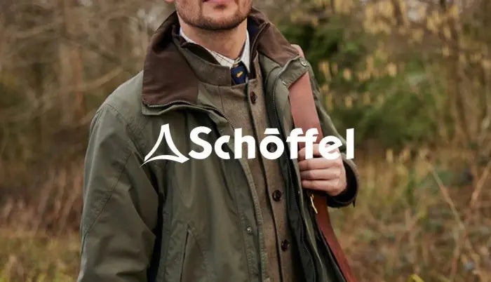 A man outdoors wearing an olive green Schöffel jacket with a brown collar, holding a brown leather strap, with the Schöffel logo overlaid across the center.